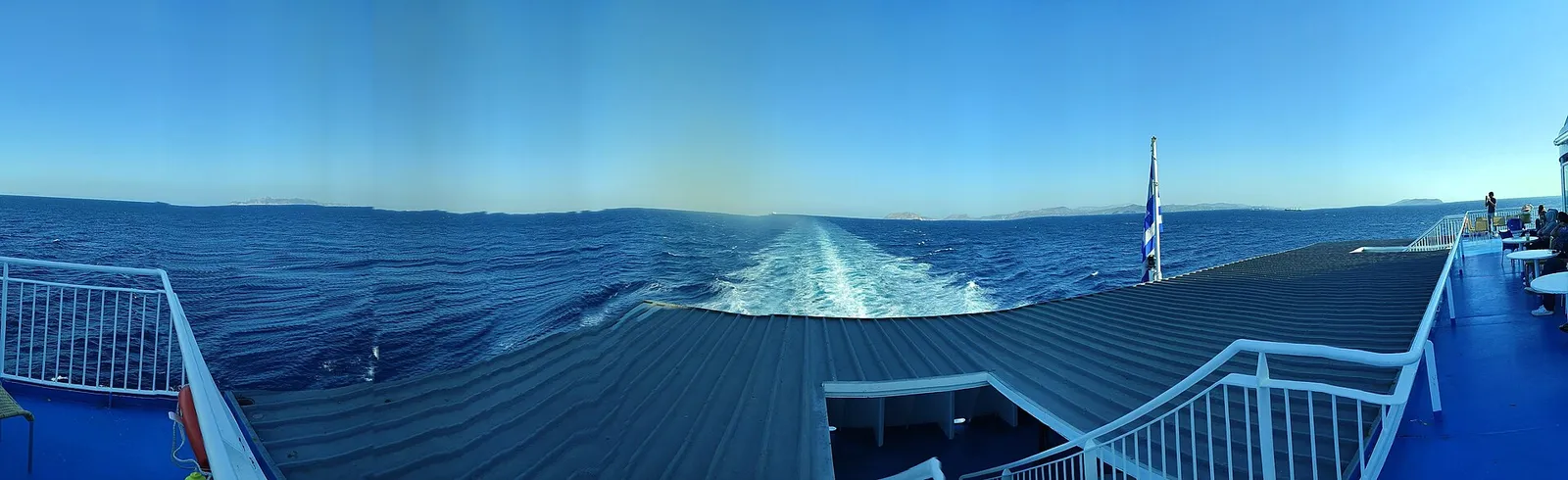 נוסעים יושבים על הסיפון הפתוח של מעבורת בים האגאי ביוון עם נוף לאי באופק