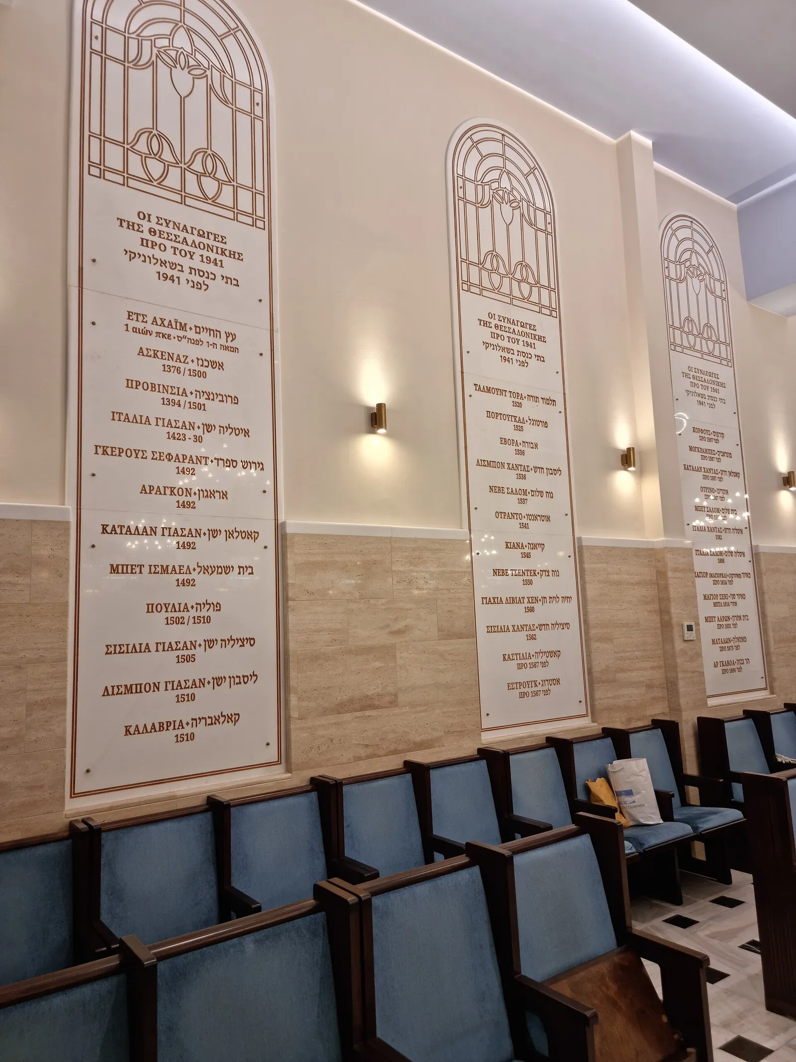 פנים בית הכנסת יד לזיכרון בסלוניקי שביוון עם ספסלי תפילה ולוחות שיש, לב הקהילה היהודית הפעילה של העיר