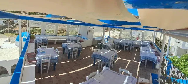 מרפסת מקורה ביריעות צל, עם שולחנות במפות משובצות כחול ולבן