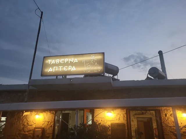 שלט מואר ביוונית על גג מבנה אבן עם פנסים דולקים בשעת דמדומים