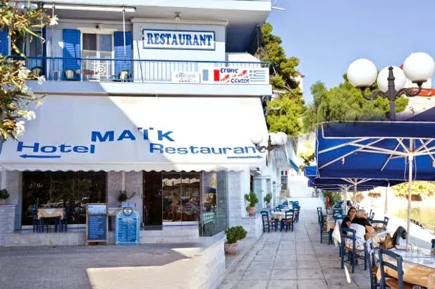 מבנה לבן כחול עם שלטים, סוככים כחולים ושולחנות על המדרכה לצד פנסי רחוב