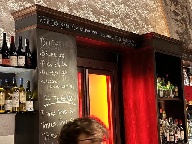 דלפק בר עם לוח גיר של מנות ויין בכוס, ובקבוקים על המדפים