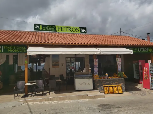 חזית טברנה עם גג רעפים, שולחנות בחוץ ודוכן תפוזים בכניסה תחת שמיים מעוננים