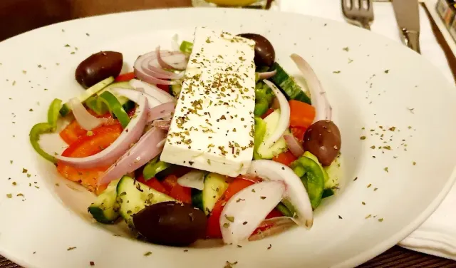 צלחת סלט עם פרוסת גבינה לבנה, זיתים, עגבנייה, מלפפון ובצל סגול