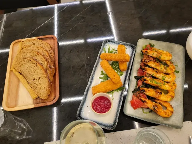 פרוסות לחם, מקלות גבינה מטוגנים ושרימפס צלויים על משטח שיש כהה
