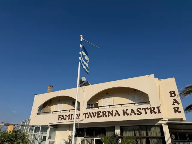מבנה בהיר עם קשתות ודגל יוון מתנופף מעליו, תחת שמיים כחולים