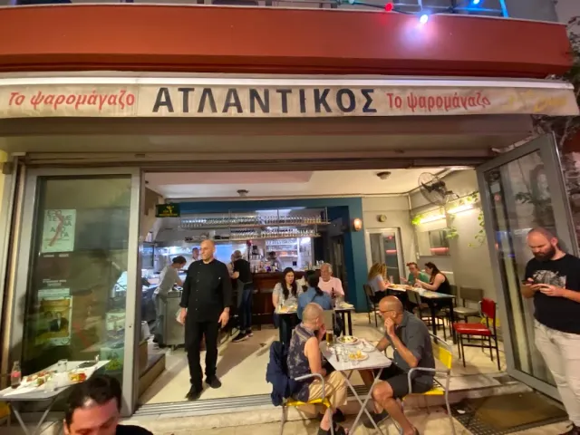חזית פתוחה בלילה עם שלט אדום, שולחנות קטנים וסועדים במדרכה
