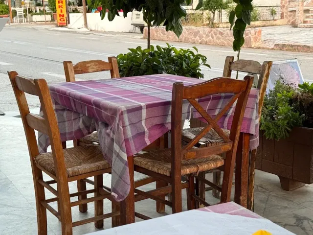 שולחן בחוץ במפה משובצת סגולה, כיסאות עץ עם מושבי קש ועציצים לצדו