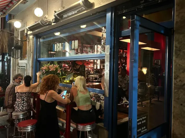 אנשים על שרפרפים אדומים מול חלון בר פתוח לרחוב בערב