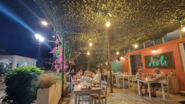 סועדים בערב מתחת לגג צמחייה עם נורות תלויות וקיר כתום מואר