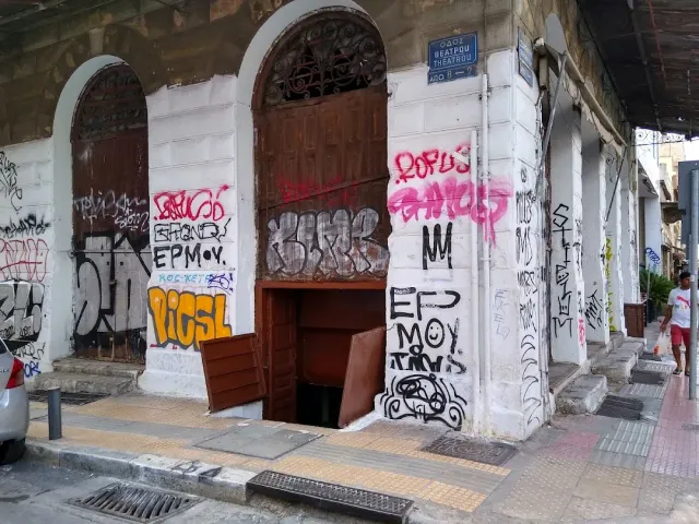 פינת בניין ישן מכוסה גרפיטי, עם פתח מרתף פתוח במדרכה