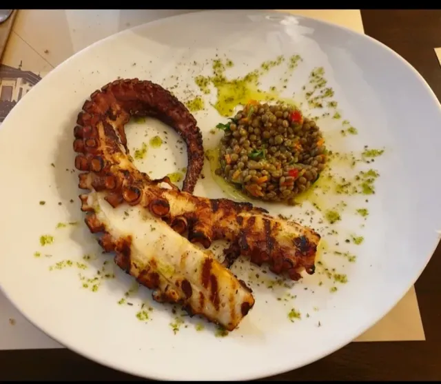זרוע תמנון צלויה בצלחת לבנה, לצד סלט עדשים ושמן ירוק