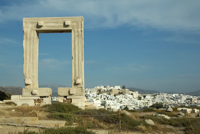 שער שיש עתיק העומד לבדו על גבעה, ומאחוריו עיירה לבנה והים