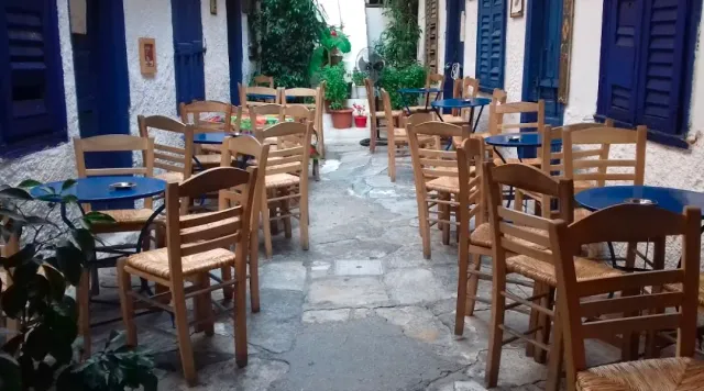 סמטה מרוצפת עם כיסאות קש ושולחנות כחולים, ליד תריסים כחולים