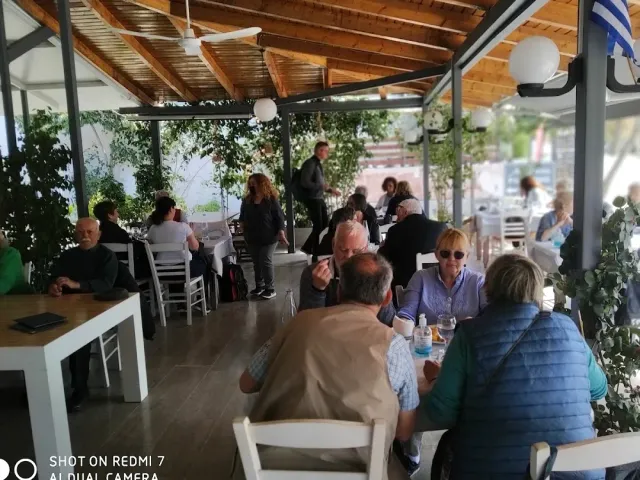 ורנדה מקורה עם תקרת עץ, שולחנות לבנים וסועדים רבים תחת מאווררים