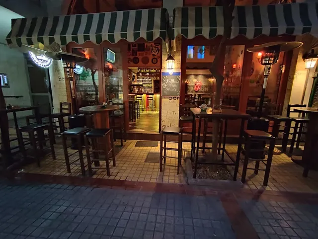 שולחנות ושרפרפים גבוהים מתחת לסוככים מפוספסים ירוק לבן, מול בר מואר בלילה
