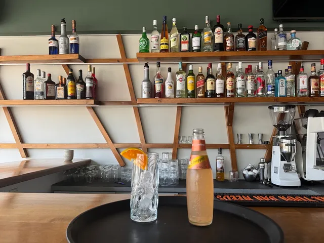 מדפי עץ עמוסי בקבוקי משקאות מעל דלפק בר, עם כוס קוקטייל ומכונת קפה