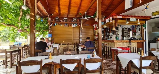 טברנה מקורה בקורות עץ וגפן, שולחנות במפות לבנות, כיסאות עץ ודלפק בר