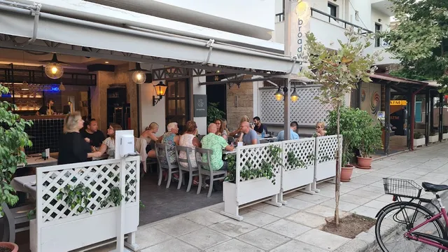 סועדים יושבים במרפסת מסעדה מגודרת בסורג לבן על מדרכה עירונית