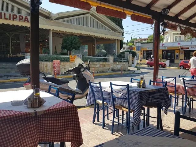מרפסת מקורה עם מפות משובצות וכיסאות כחולים, וקטנוע חונה ברחוב