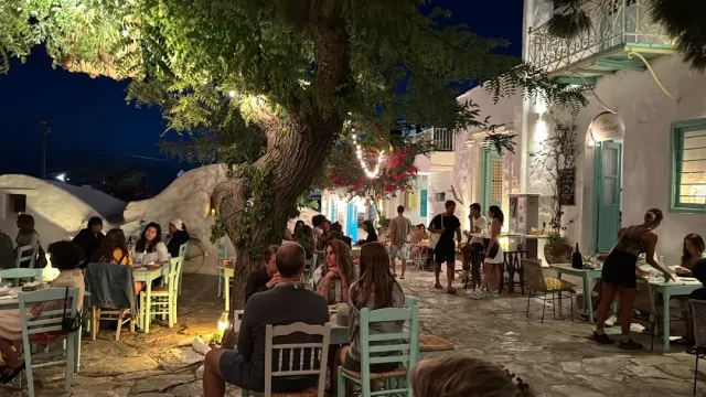כיכר כפרית בלילה עם עץ גדול, כיסאות טורקיז וסועדים רבים