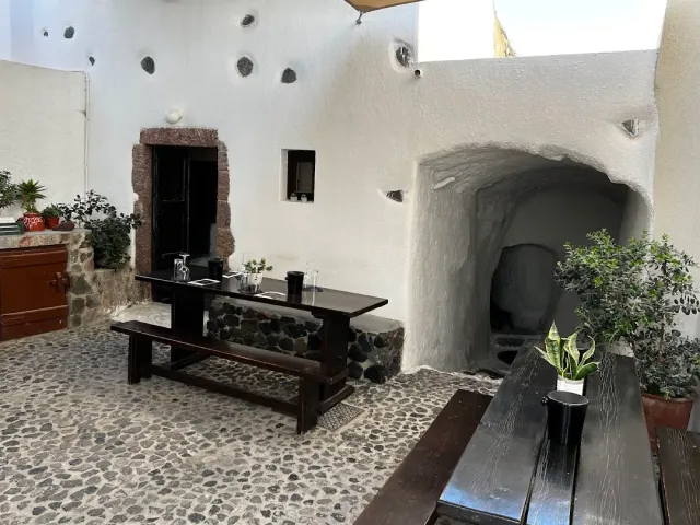 חצר מסוידת עם ריצוף חלוקים, שולחנות עץ כהים וכניסה מקומרת למערה