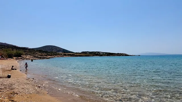 חוף חולי רחב עם מים צלולים ורדודים, וגבעות נמוכות ברקע