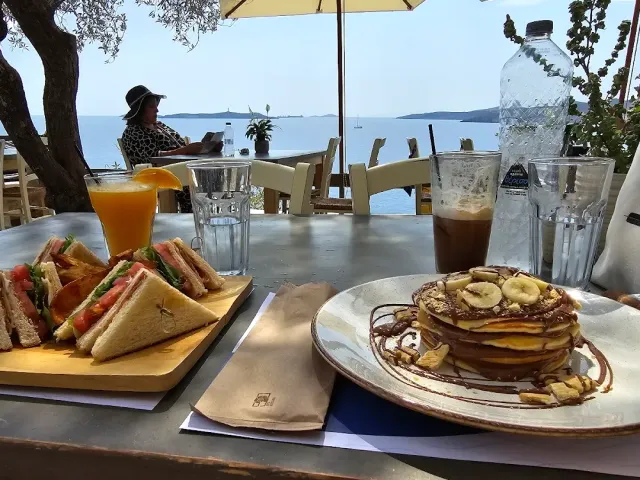 כריכים משולשים, פנקייקים עם בננה ומיץ תפוזים על שולחן מול הים