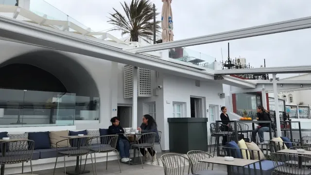 טרסה לבנה עם סככה נפתחת, ספות, שולחנות עגולים ודקל ברקע