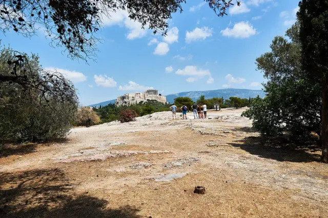 מדרון עפר וסלע עם מטיילים, ובמרחק גבעת האקרופוליס