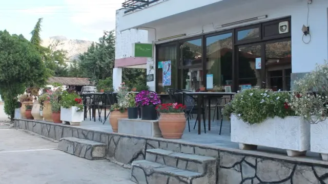 טרסה עם שולחנות מתכת והרבה עציצים פורחים על קיר אבן, מול מבנה לבן