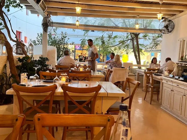 מרפסת מקורה עם קורות עץ, מנורות תלויות ושולחנות שסועדים יושבים סביבם